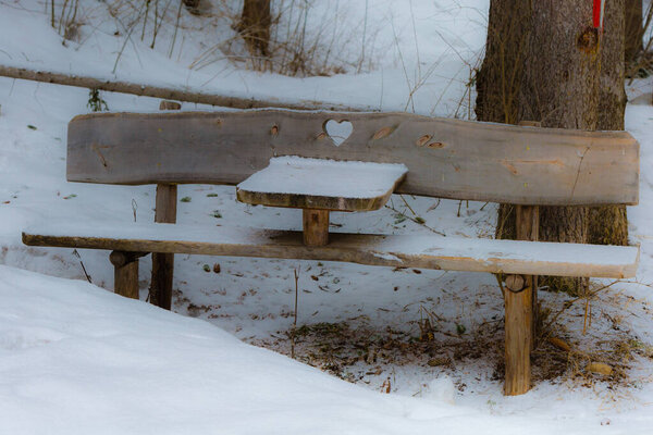 Wooden Bench with Heart Carved in wood Among Fresh Snow in Italian Dolomites Mountains.