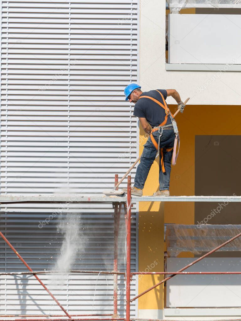 Worker with Blue Hardhat at Work on a Scaffold in a Building Site for the Construction of a Building.