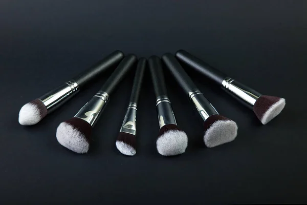 Cepillos de maquillaje profesionales sobre fondo negro, tela natural — Foto de Stock