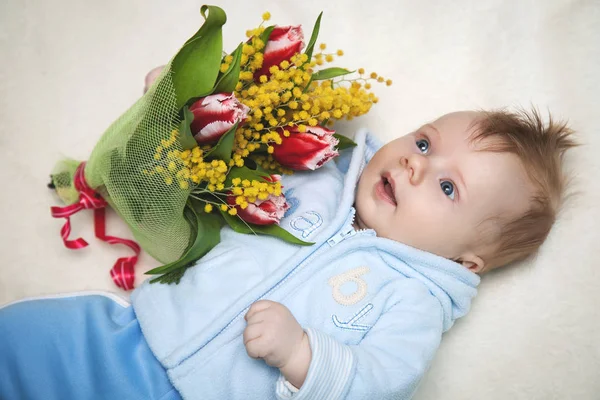 Kleine jongen liggend op het bed met een boeket van tulpen — Stockfoto