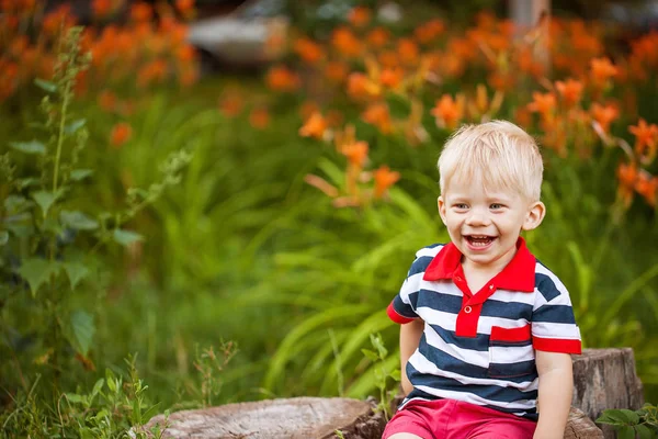 Kleine jongen zit op een boomstronk en smeeisya op een achtergrond van Oranje lelies — Stockfoto