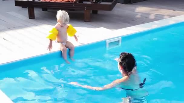 Petit garçon sautant dans la piscine avec des brassards jaunes , — Video