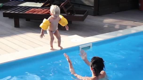 Niño saltando a la piscina con brazaletes amarillos , — Vídeos de Stock