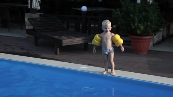 Un niño pequeño al lado de la piscina con brazaletes amarillos — Vídeo de stock