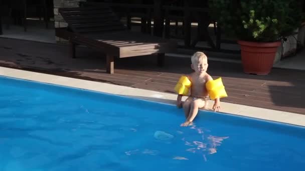 Egy kisfiú a sárga karszalagok a medence mellett — Stock videók