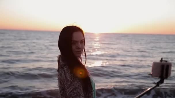 Jovem menina bonita fazendo selfie na praia do mar em um fundo quente pôr do sol — Vídeo de Stock