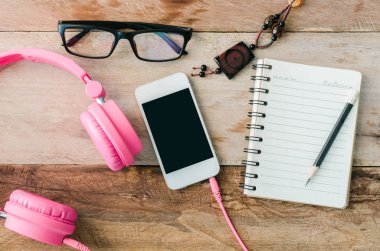 Bir defter, akıllı telefon, kulaklık, gözlük ile ahşap bir masa yüzeyine,