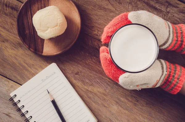 Guanto a mano che tiene un bicchiere di latte caldo a colazione e matita per notebook sul pavimento in legno — Foto Stock