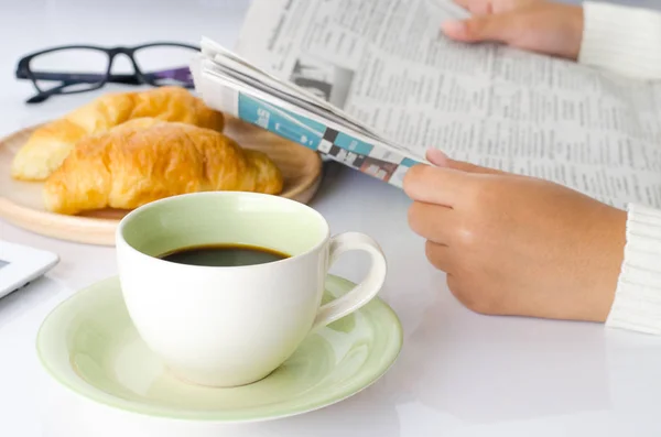 Kubek kawy na biurku i czytanie gazety. — Zdjęcie stockowe