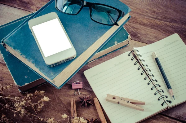 Smartphone está en un libro Incluir lápiz está en un cuaderno, gafas en el fondo de madera . —  Fotos de Stock