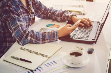 Kadın eli notebook klavye üzerinde yerleştirilen ve akıllı telefon tutarak ahşap bir masa üzerinde bir çalışma cihazla yerleştirilir ve bir bardak kahve yerleştirilmiş .