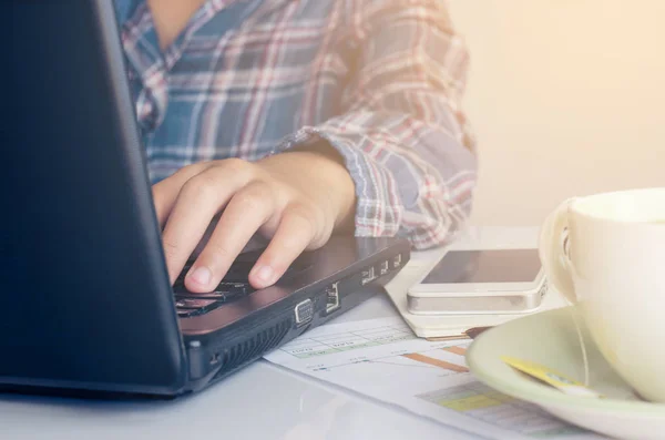 Die Hand der Frau hält Smartphone, Kreditkarte und Notizbuch auf einem Holztisch mit einem funktionierenden Gerät und wird in einen gläsernen Kaffeebecher gelegt. — Stockfoto