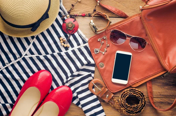 Accessories for teenage girl on her vacation. Straw hat, stylish sunglasses, brown leather bag, red shoes and costume on wooden floor.