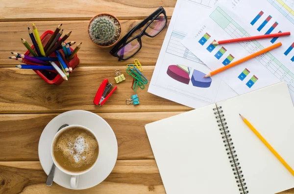 Xícara de café, gráfico, caneta, notebook e acessório para trabalho em mesa de madeira . — Fotografia de Stock