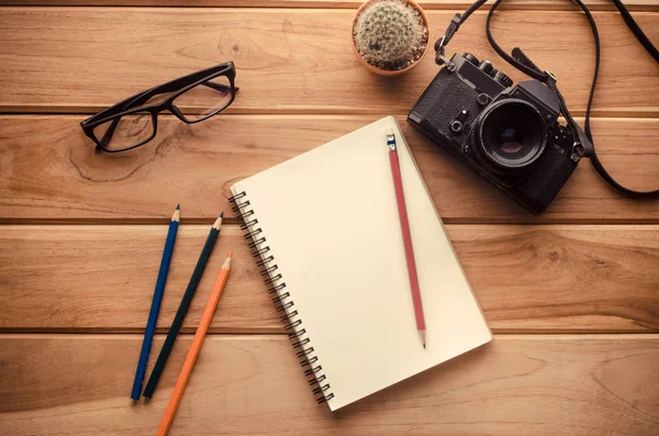 Macchina fotografica, taccuino, matita e occhiali su tavola di legno — Foto Stock