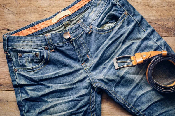 Modré džíny s koženým páskem na dřevěné pozadí — Stock fotografie