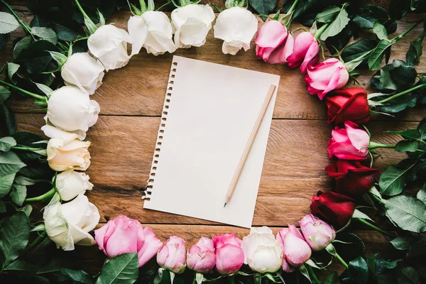 Colorful roses lined up on a wooden floor paper and pencil with space for writing your message.