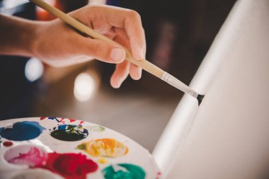 Kapalı kız paleti tutuyor ve boya kullanarak tuvale çiziyor. 