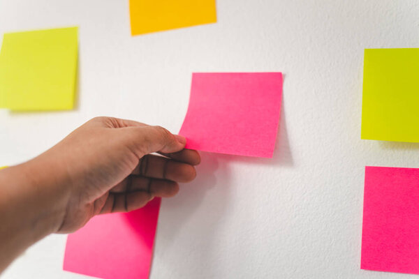 The hand is holding the post it notes attached to the wall. Concept brainstorming, share idea.