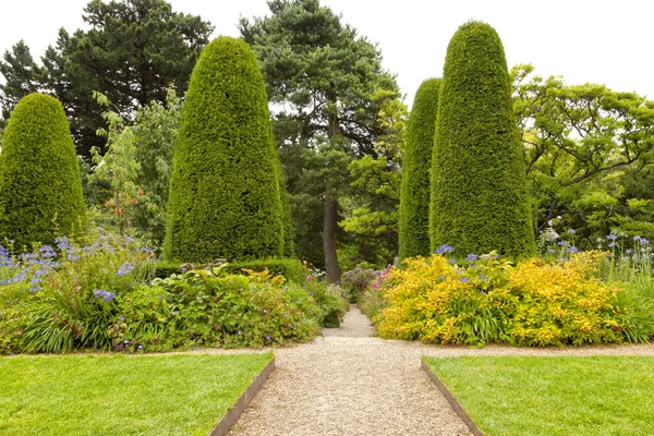 Percorso a piedi attraverso un giardino estivo paesaggistico con fiori, alberi, conifere — Foto Stock