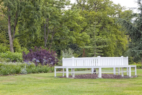 Weiße Holzbank im angelegten englischen Garten mit altem Baumbestand und Sträuchern — Stockfoto