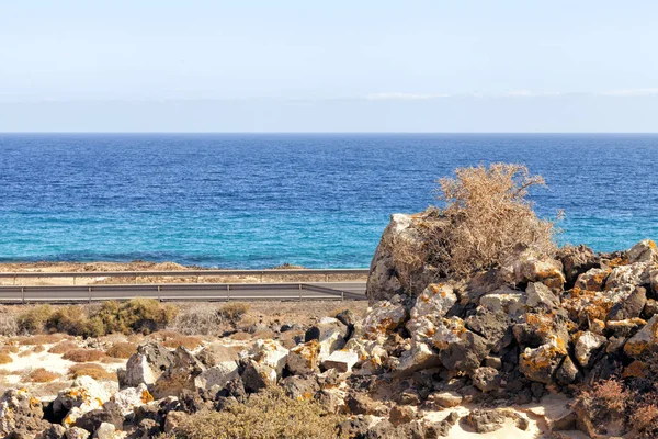 Coastline road, pile of colorful volcanic rocks on edge of desert dune park, Fuerteventura, Canary Islands, Spain .