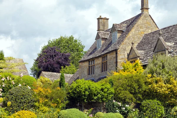Gözlerden uzak kireç taş Cotswold house İngilizce ülkede arduvaz çatılı herdem yeşil bitkiler, ağaçlar, çiçekler, pembe güller, güneşli bir yaz Bahçe dolu .