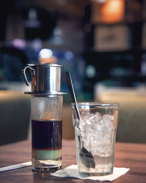 Traditional vietnamese coffee with condensed milk and glass of ice cube in moody dim cafe restaurant background