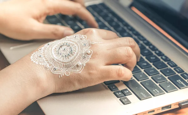 Hand typing on laptop keyboard. Woman hand with mandala design henna art. Concept of working from home.
