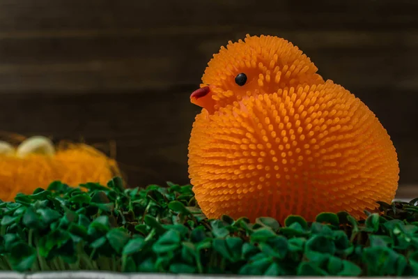 Orange toy chicken near a decorative nest with an egg on a wooden texture