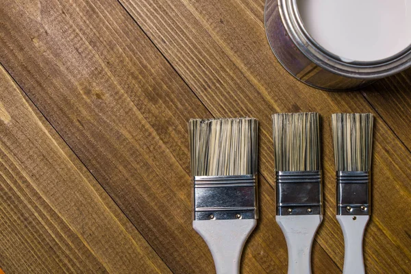 Painting brushes near a metal jar with white paint on an oak table