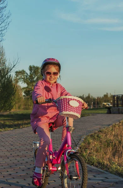 Bébé fille dans un casque rose sur un vélo à deux roues dans un parc au coucher du soleil — Photo