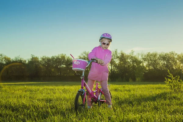 Bébé fille dans un casque rose sur un vélo à deux roues dans un parc au coucher du soleil — Photo