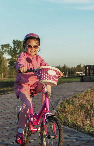 Девочка в розовом шлеме на двухколесном велосипеде в парке на закате — стоковое фото