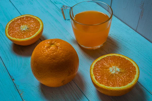Een glas verse jus d'orange met gesneden sinaasappelen op een houten tafel. Bereiding van verse jus d'orange — Stockfoto