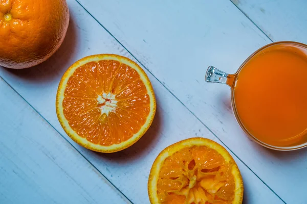 Стакан свежего апельсинового сока с нарезанными апельсинами на деревянном столе. Подготовка апельсинового сока — стоковое фото