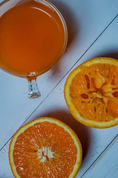 A glass of fresh orange juice with sliced oranges on a wooden table. Preparation of fresh orange juice — Stock Photo, Image