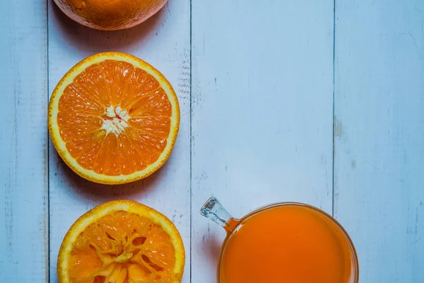 Ein Glas frischen Orangensaft mit geschnittenen Orangen auf einem Holztisch. Herstellung von frischem Orangensaft — Stockfoto