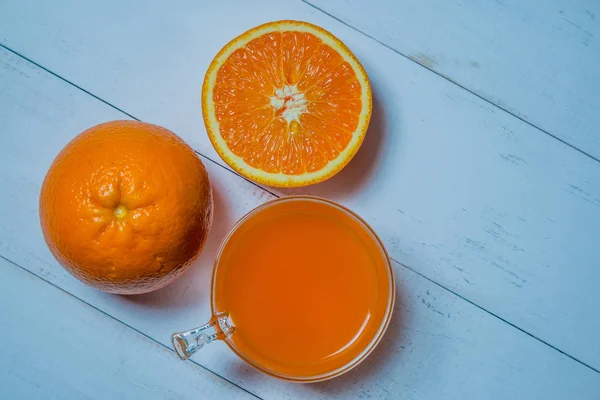 Een glas verse jus d'orange met gesneden sinaasappelen op een houten tafel. Bereiding van verse jus d'orange — Stockfoto