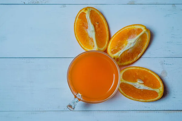 Ein Glas frischen Orangensaft mit geschnittenen Orangen auf einem Holztisch. Herstellung von frischem Orangensaft — Stockfoto