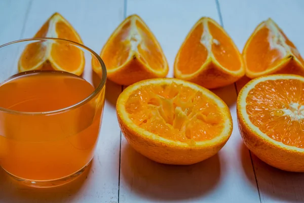 Een glas verse jus d'orange met gesneden sinaasappelen op een houten tafel. Bereiding van verse jus d'orange — Stockfoto