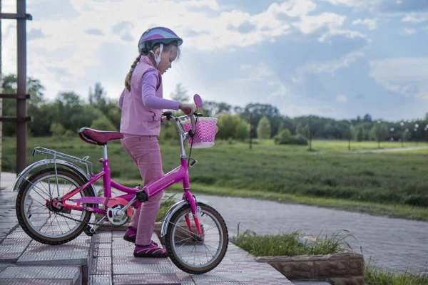 Une fillette de sept ans portant un casque rose porte seule son vélo sur les marches du parc — Photo