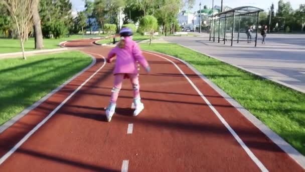 Семилетняя девочка учится кататься на роликах в летнем парке на велосипедной дорожке — стоковое видео
