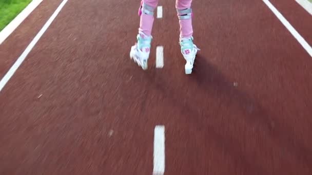 Uma menina de sete anos aprende a patinar no parque em um caminho de bicicleta — Vídeo de Stock