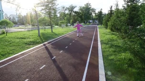 Uma menina de sete anos aprende a patinar no parque em um caminho de bicicleta — Vídeo de Stock