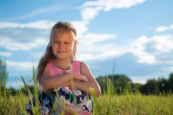 Porträt eines schönen Mädchens auf Gras in einem Park vor einem Hintergrund aus weißen Wolken und blauem Himmel — Stockfoto