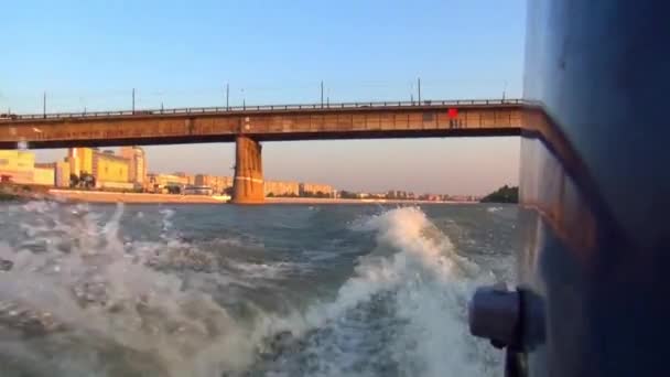 Födosöker skärare med monterad motor, på segrad kölvattnet på solnedgången, bort city bridge — Stockvideo