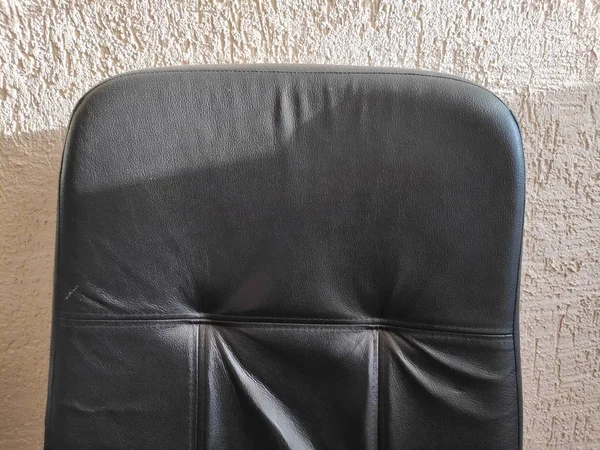 Ein unordentlicher schwarzer Lederstuhl gegen eine verputzte Wand — Stockfoto