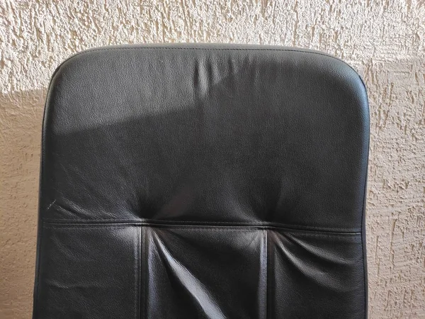 Una sedia in pelle nera disordinata contro una parete intonacata — Foto Stock