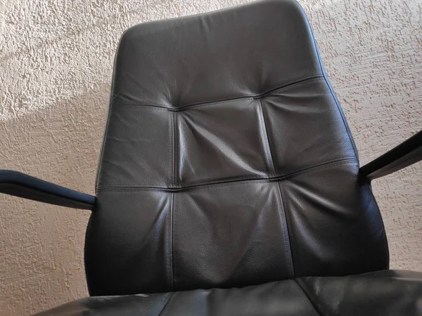 Una sedia in pelle nera disordinata contro una parete intonacata — Foto Stock